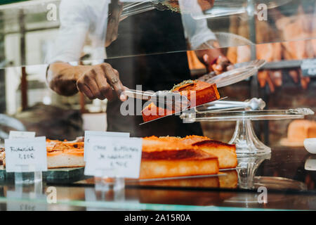 Mann bei der Arbeit in einer Bäckerei, ein Stück Kuchen auf den Teller Stockfoto
