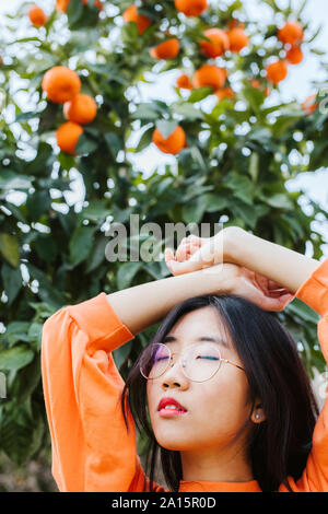 Portrait von jungen asiatischen Frau, Tangerine Baum im Hintergrund Stockfoto