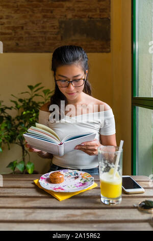 Junge Frau am Tisch sitzend ein Buch lesen Stockfoto