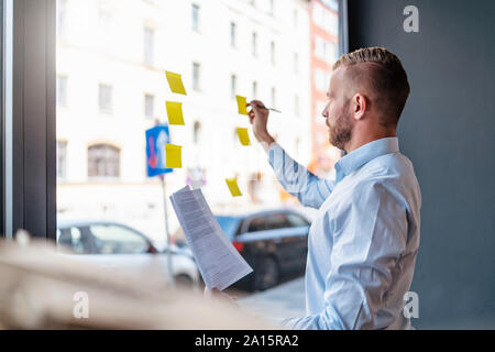 Geschäftsmann schreiben auf Haftnotizen an der Glasscheibe Stockfoto