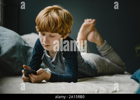 Portrait von rothaarigen Jungen liegen auf der Couch am Handy suchen Stockfoto