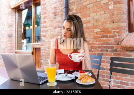 Junge blogger an Street Cafe sitzen an Laptop suchen Stockfoto