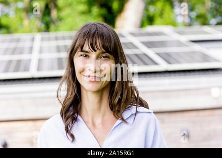 Portrait von lächelnden Frau vor einem Haus mit Solarzellen auf dem Dach Stockfoto