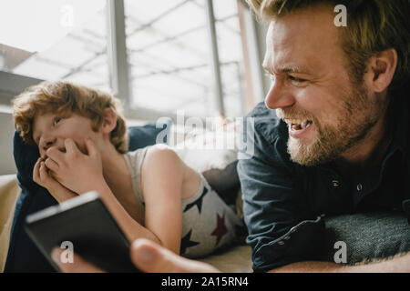 Vater und Sohn liegen auf der Couch Spaß mit Handy Stockfoto