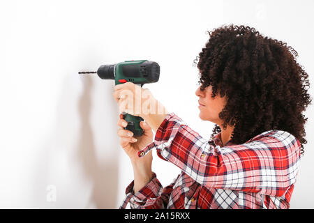 Frau mit Handbohrmaschine, Kennzeichnung mit Bleistift an der Wand Stockfoto