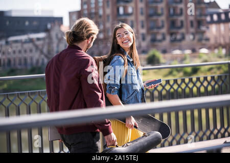 Glückliches junges Paar mit Skateboard zu Fuß auf einer Brücke Stockfoto