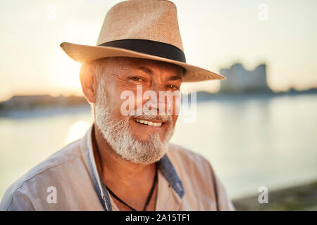 Porträt eines lächelnden älteren Mann, der Sommer hat im Riverside bei Sonnenuntergang Stockfoto