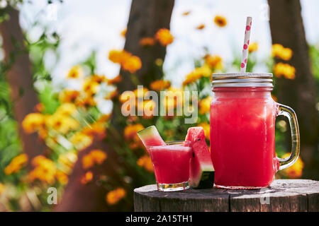 Nahaufnahme der frische Wassermelone Cocktail in Glas und Mason jar auf Baumstumpf im Garten Stockfoto