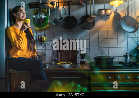 Junge Frau auf Arbeitsplatte in der Küche zu Hause sitzen einen Kaffee genießen. Stockfoto