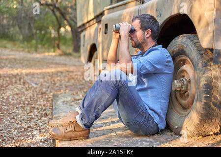 Man sitzt von Geländewagen, Blick durch ein Fernglas Stockfoto