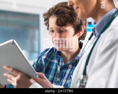 Frau Doktor, ein junger männlicher Patient sein Labor die Ergebnisse auf einem digitalen Tablet in der Klinik Stockfoto