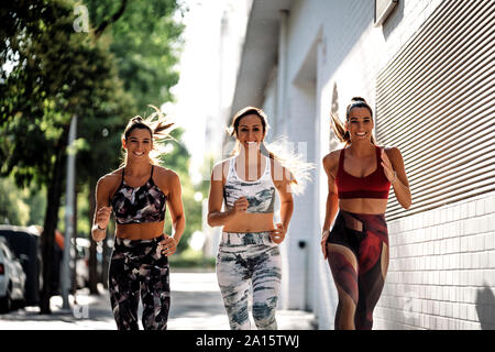 Drei glückliche sportliche junge Frauen in der Stadt läuft Stockfoto
