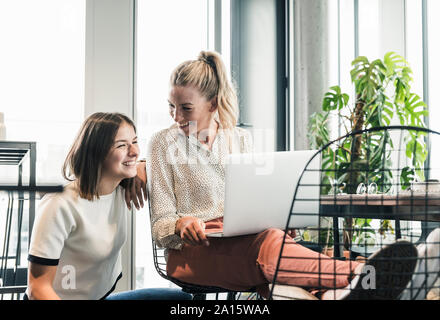 Zwei glückliche casual Unternehmerinnen mit Laptop im Büro Stockfoto