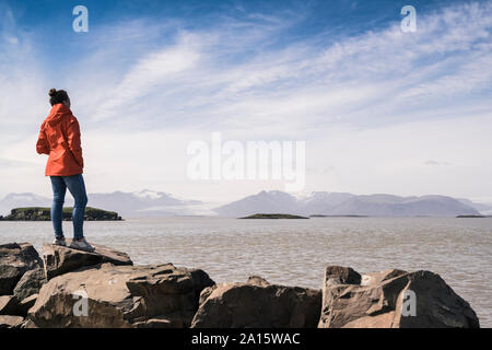 Junge Frau standig Felsbrocken, mit Blick auf das Meer, South East Iceland Stockfoto