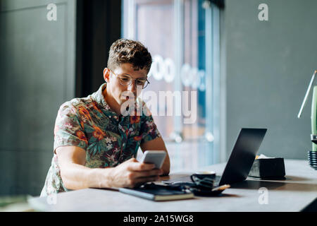 Junger Mann im Cafe sitzen, mit samrtphone und Laptop Stockfoto