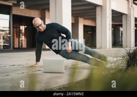 Portrait von lächelnden Mann tun Pushups während an Laptop suchen Stockfoto