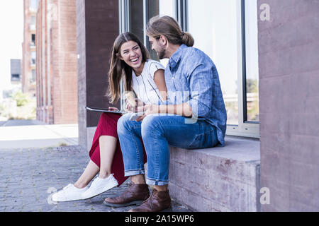 Junges Paar sitzt auf der Fensterbank bei Verwendung eines Tablet Gebäude Stockfoto