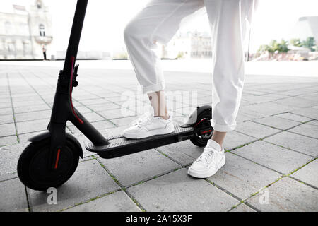 Junge Frau mit e-Scooter, moderne Gebäude im Hintergrund Stockfoto