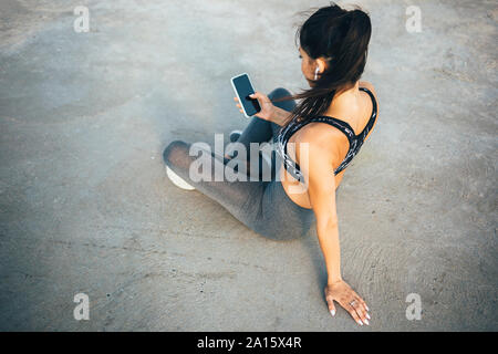 Frau mit Smartphone und In-ear während des Trainings, sitzend auf einem Pier Stockfoto