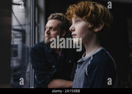 Junge und sein Vater auf der Suche aus dem Fenster an regnerischen Tag Stockfoto