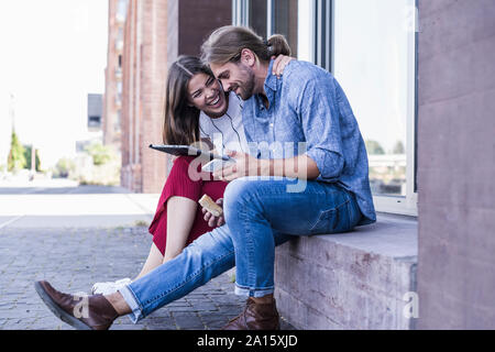 Junges Paar sitzt auf der Fensterbank bei Verwendung eines Tablet Gebäude Stockfoto