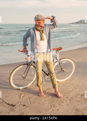 Barfuß Mann stand mit Fixie bike am Strand mit Blick auf Abstand Stockfoto