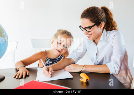 Lehrer, Schülerin am Schreibtisch Schreiben auf Papier Stockfoto