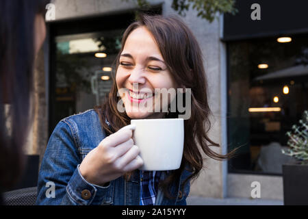 Glückliche junge Frau lachend mit geschlossenen Augen und Holding Kaffeetasse in Outside cafe in Madrid, Spanien Stockfoto