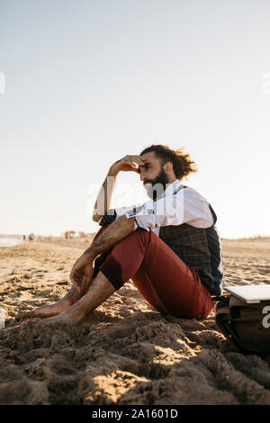 Nachdenklich gut gekleideter Mann sitzt auf einem Strand Stockfoto