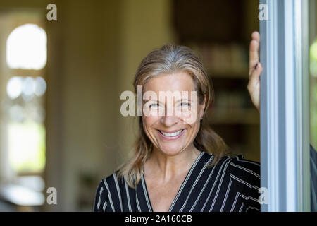 Portrait von lächelnden reife Frau stehend an geöffneten Terrasse Tür Stockfoto