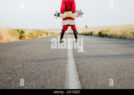 Niedrige Abschnitt von Santa Claus mit einem Longboard auf Landstraße Stockfoto