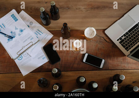 Bier Flaschen, Gläser, Dokumente, Smartphones und Laptops auf Tisch Stockfoto