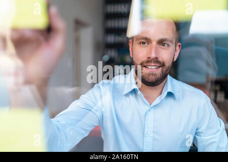 Geschäftsmann schreiben auf Haftnotizen an der Glasscheibe Stockfoto