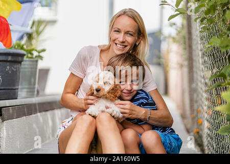 Portrait von Mutter und Sohn Kuscheln mit niedlichen Hund Welpe Stockfoto