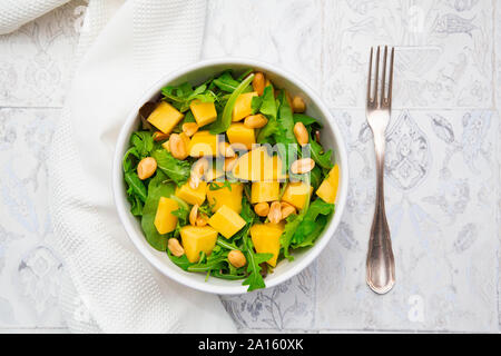 In der Nähe von frischem Salat in der Schüssel durch die Serviette und Gabel auf gefliestem Boden Stockfoto