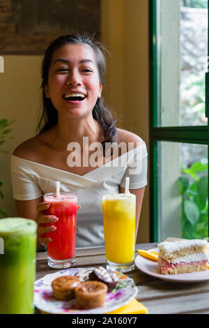 Lachende junge Frau trinkt einen Smoothie in einem Cafe Stockfoto