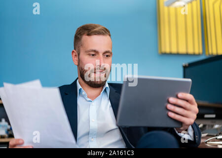 Geschäftsmann mit Papieren und Tablet am Schreibtisch im Büro Stockfoto