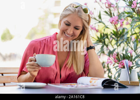 Portrait von lächelnden blonde Frau trinkt Kaffee im Café lesen Magazin Stockfoto