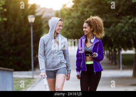 Zwei lächelnde sportliche junge Frauen wandern im Park nach dem Workout Stockfoto