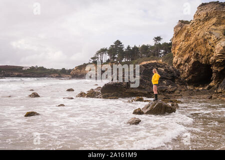 Frau tragen gelbe Regenjacke stehen auf Rock am Strand Stockfoto