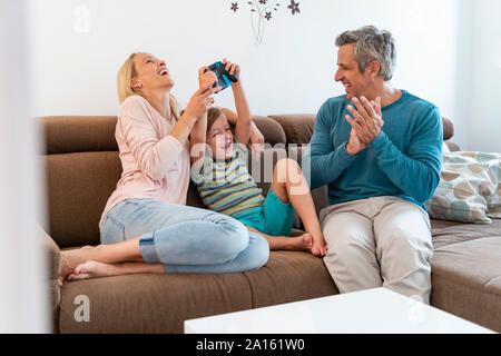 Glückliche Eltern mit Sohn spielen Video Game auf der Couch zu Hause Stockfoto