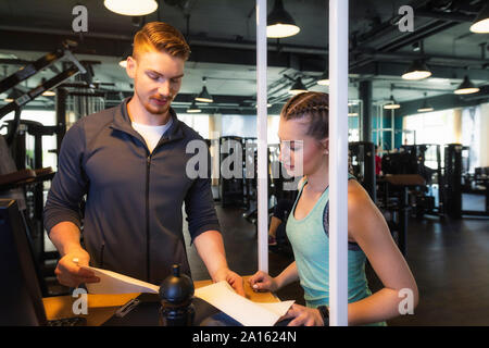 Junge Frau und Personal Trainer diskutieren Plan im Fitness Gym Stockfoto