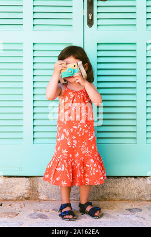 Kleine Mädchen spielen mit Holzspielzeug Kamera das Tragen der roten Kleid mit Blumenmuster Stockfoto