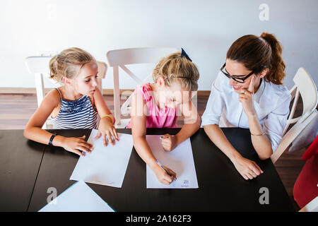 Lehrer am Schreibtisch sitzend mit zwei Schülerinnen Schreiben auf Papier Stockfoto