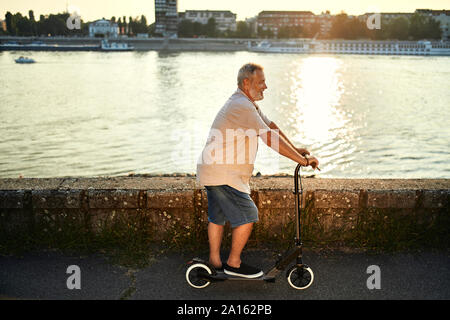 Älterer Mann, e-Scooter, die am Flußufer Stockfoto