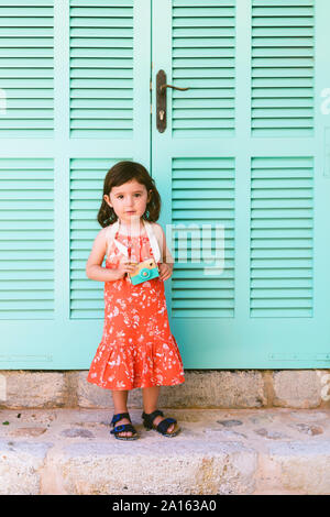 Portrait von kleinen Mädchen mit Holzspielzeug Kamera das Tragen der roten Kleid mit Blumenmuster Stockfoto