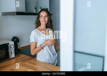 Junge Frau, die in der Küche mit einem Glas Orangensaft Stockfoto