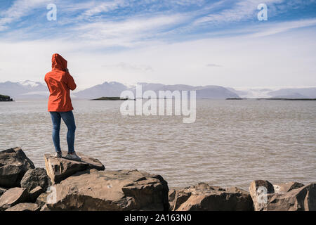 Junge Frau standig Felsbrocken, mit Blick auf das Meer, South East Iceland Stockfoto