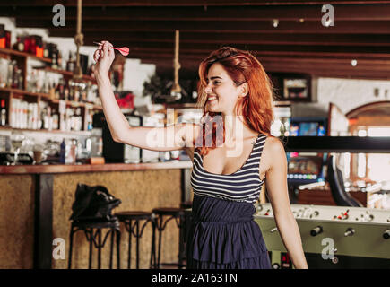 Glückliche junge Frau spielen Darts in einer Sports Bar Stockfoto