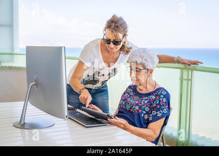 Ältere Frau mit Tablet auf der Terrasse, von ihrer Tochter geholfen Stockfoto